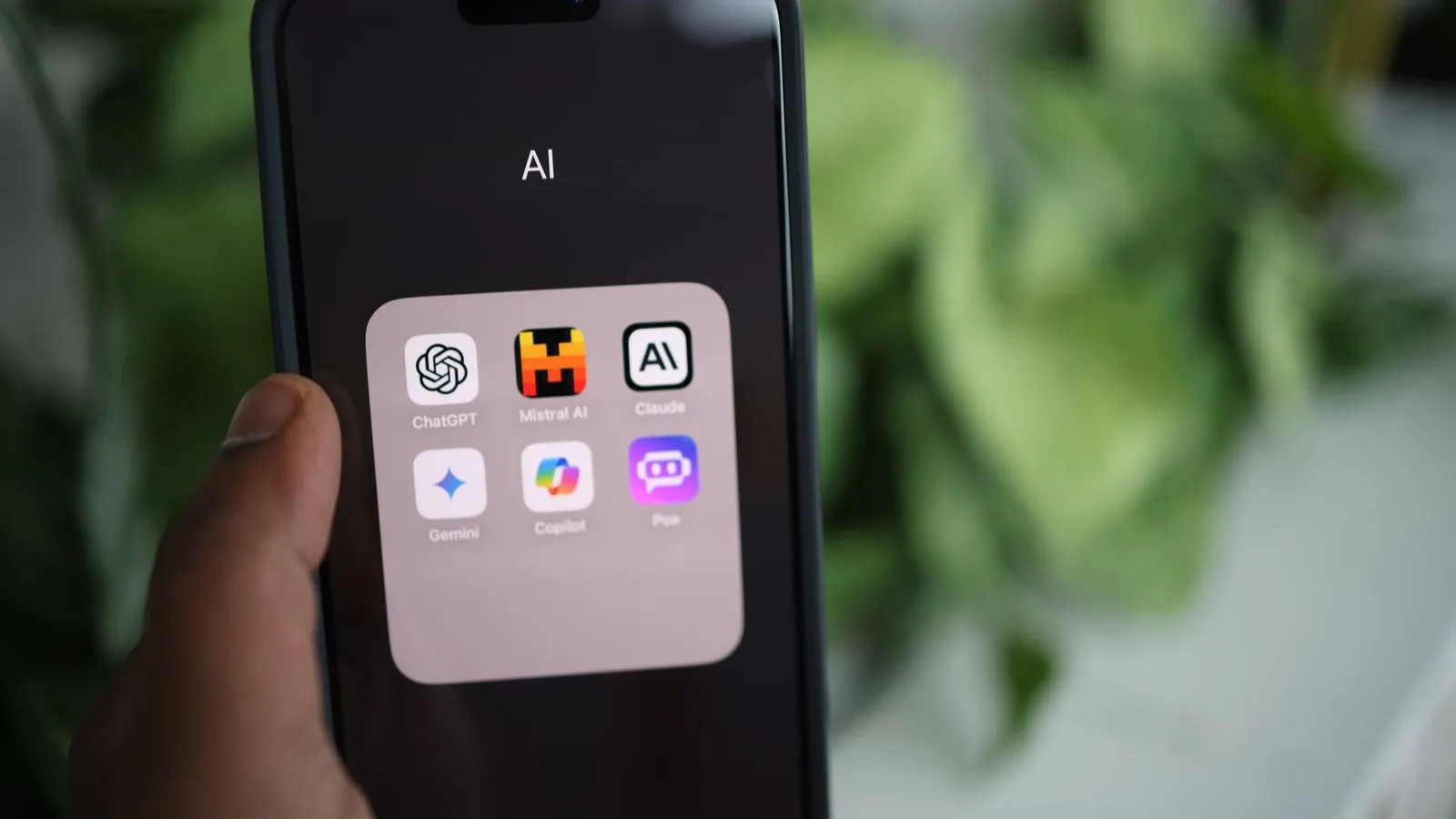 A hand holding a phone open to a folder of AI apps including ChatGPT, Gemini and Claude